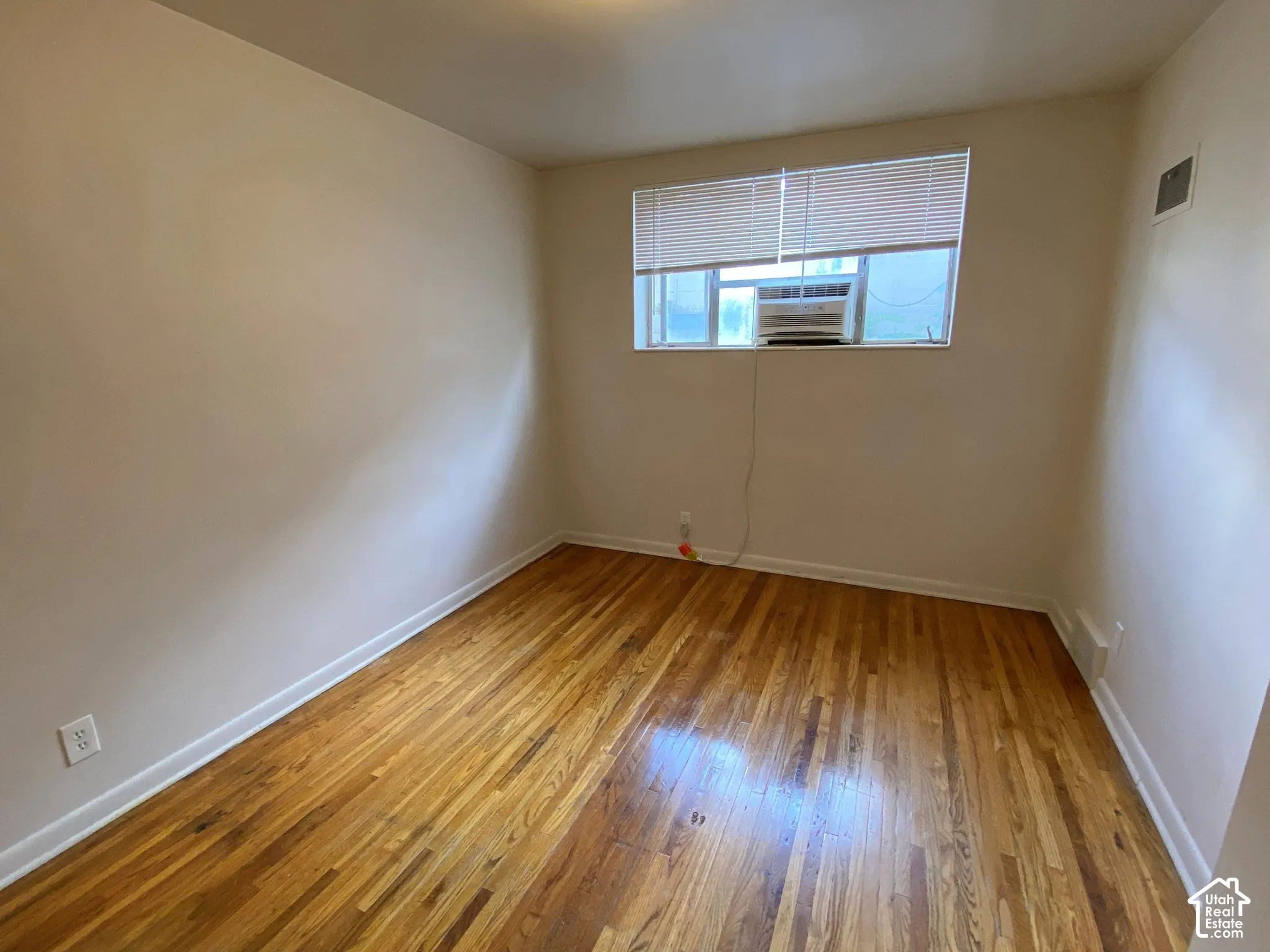Wood-finish flooring with white trim, neutral wall finishes, and a window with blinds
