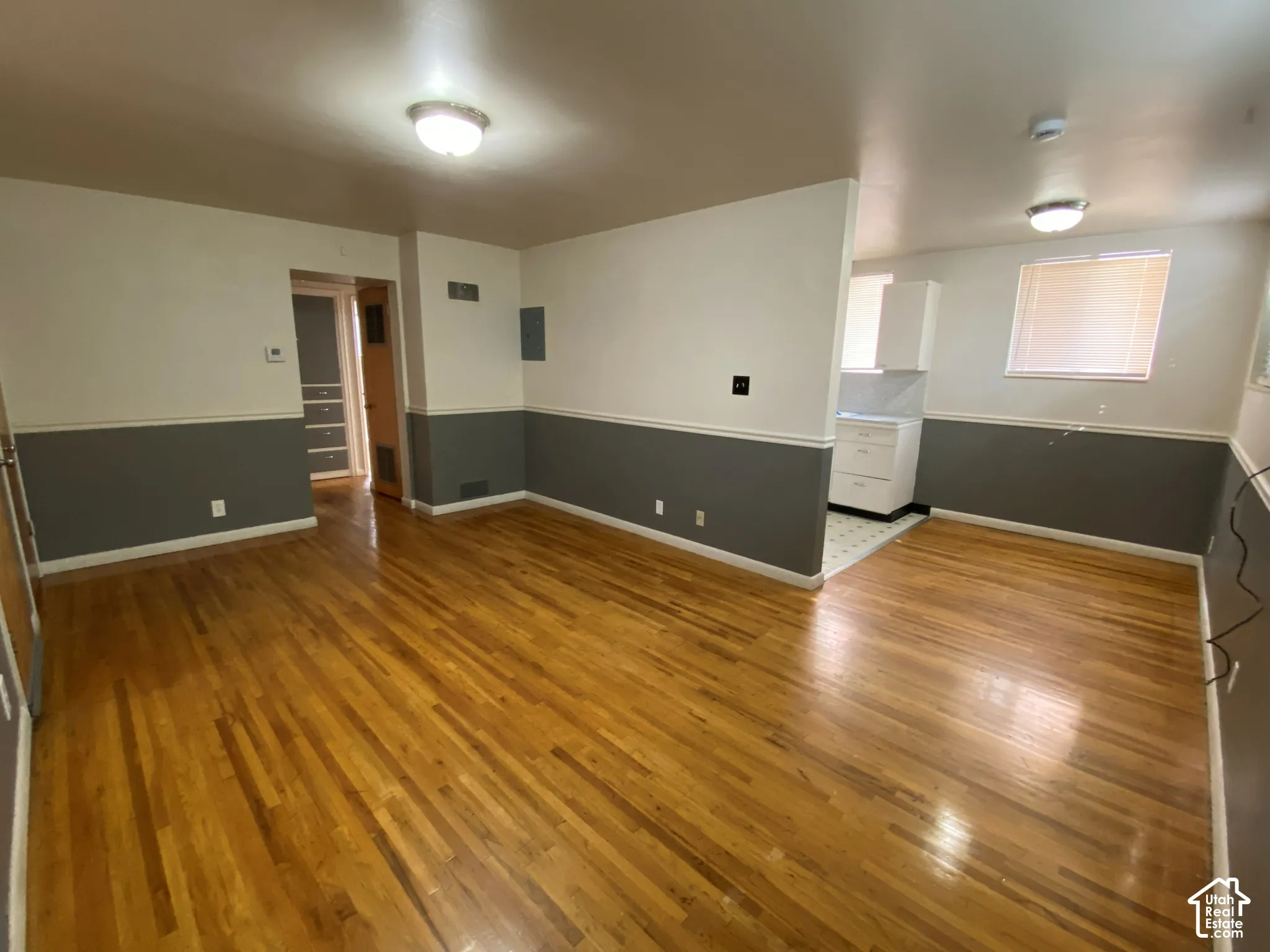 Wood-finish flooring throughout, two-tone wall paint, recessed lighting, and a kitchen area with white cabinetry and tile flooring