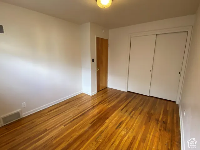 Hardwood flooring, white walls, wood-finish door, and sliding closet doors