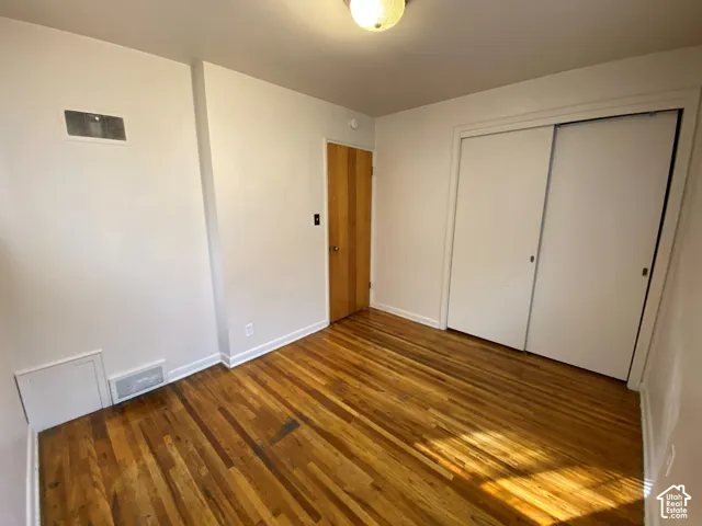 Hardwood flooring, white painted walls, natural wood-finish door, and white sliding closet doors