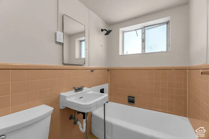 Bathroom featuring a wall-mounted sink, a bathtub with a shower fixture, and a window
