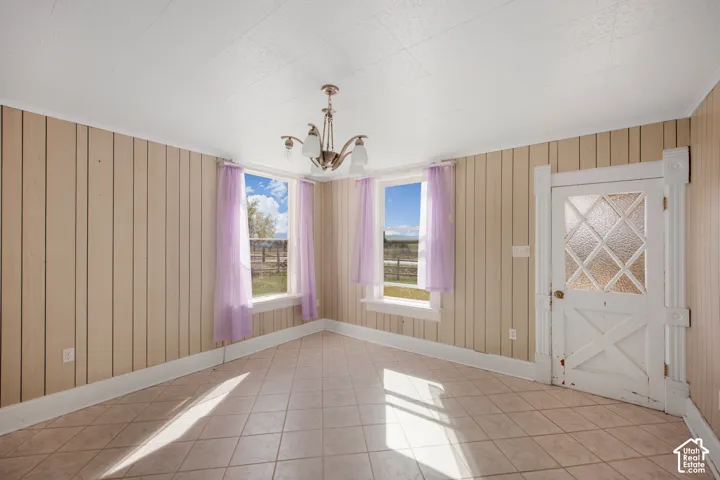 Tile flooring, vertical wall paneling, two windows with trim, a decorative ceiling light fixture, and a paneled door with frosted glass