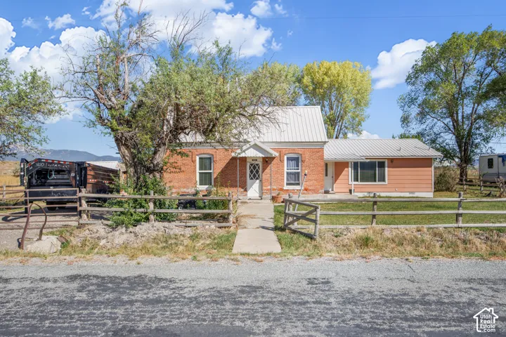 Red brick exterior, white trim windows, white metal roof, wood fence, mature trees