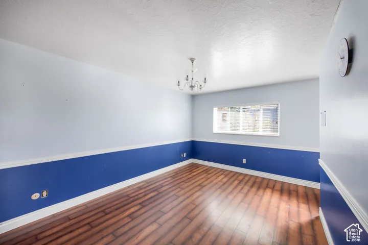 Wood-finish flooring, single window with blinds, and an overhead chandelier light fixture