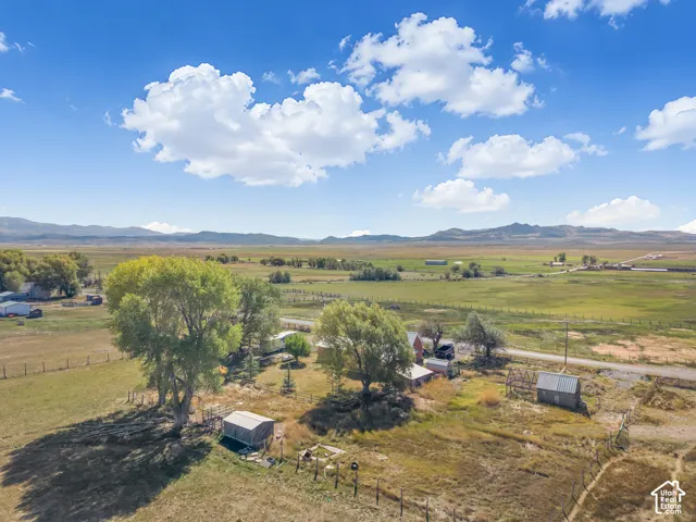 Expansive property featuring multiple structures, mature trees, open fields, and mountain scenery