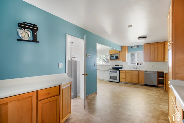 Kitchen featuring wood-finish cabinetry, white countertops, a stainless steel dishwasher, and a stainless steel oven/range