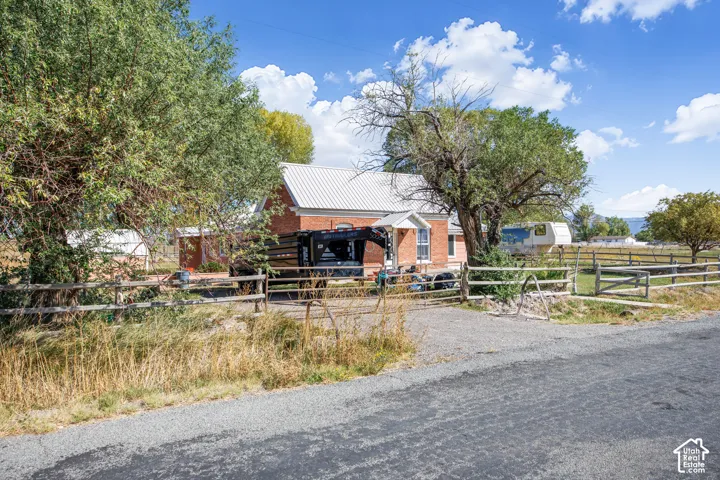 Brick exterior, metal roof, mature trees, gravel driveway, and wood fencing
