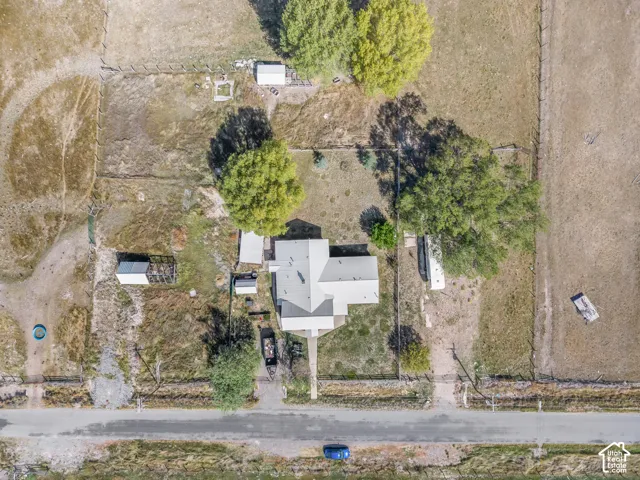 Single-story residence with a gray shingle roof, mature trees, and multiple outbuildings