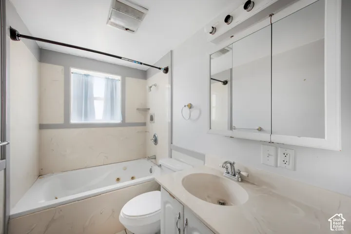 Jetted bathtub with tiled surround, single vanity with integrated sink, tri-panel mirrored medicine cabinet, and wall-mounted light fixture