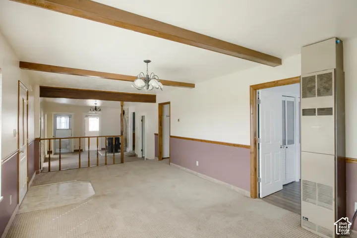 Exposed ceiling beams, chandelier lighting, and a partial wall with wood railing create distinct areas