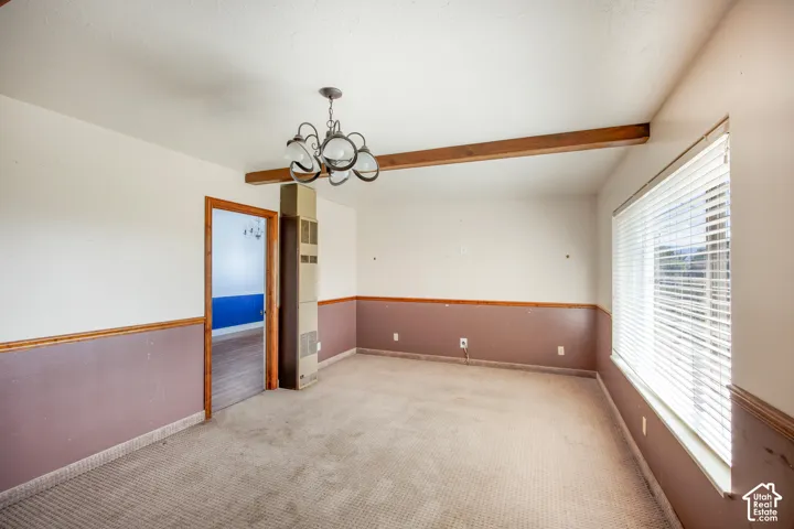 Exposed wood ceiling beam, chandelier lighting fixture, wall-to-wall carpeting, and window with blinds