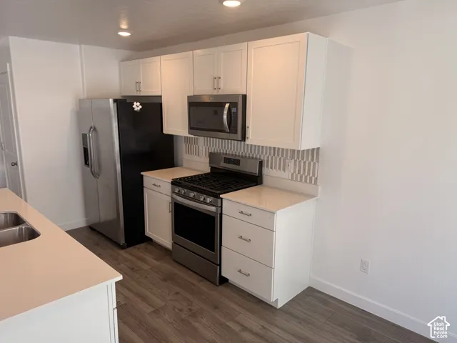 White shaker cabinetry, stainless steel appliances, wood-finish flooring, light-toned countertops, and mosaic tile backsplash