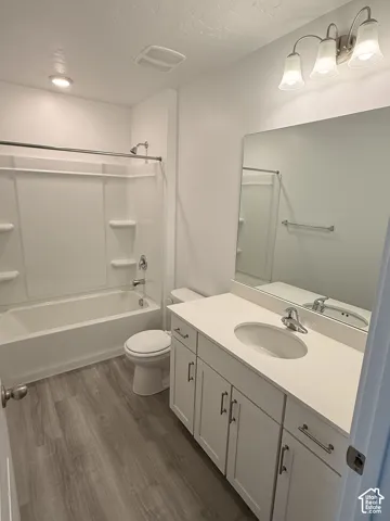 Full bathroom featuring a white vanity with a single basin sink, light-toned countertop, and wood-finish flooring