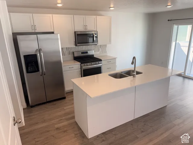 Open-concept kitchen with white cabinetry, stainless steel appliances, and wood-finish flooring