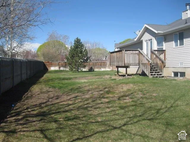 Spacious backyard featuring a wood deck with stairs, a sliding glass door entry, and perimeter fencing