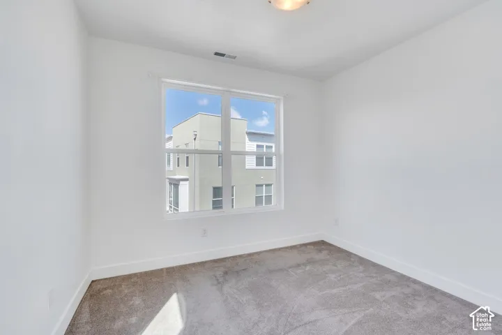 Neutral white walls, gray carpet flooring, and a single window with a white frame