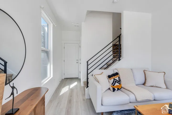 Light wood-finish flooring, white walls, white paneled door, and a staircase with black metal railings