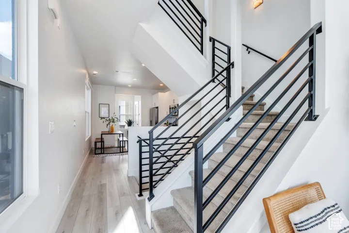 Modern black metal stair railing, light wood-finish flooring, recessed lighting, and white walls