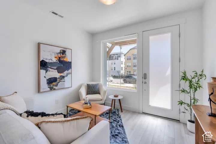 Light-toned wood-finish flooring, white walls, large window, and a door with a frosted glass panel