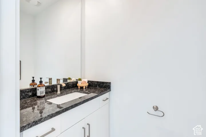 Vanity featuring a dark stone countertop, integrated rectangular sink, single-handle faucet, and white cabinetry with brushed nickel hardware