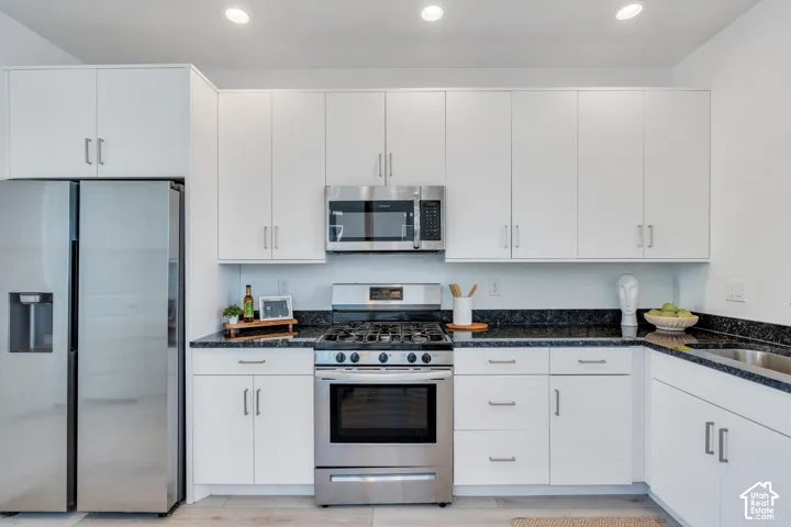 White cabinetry with brushed nickel hardware, stainless steel appliances, black countertops, and a stainless steel sink with a single-handle faucet