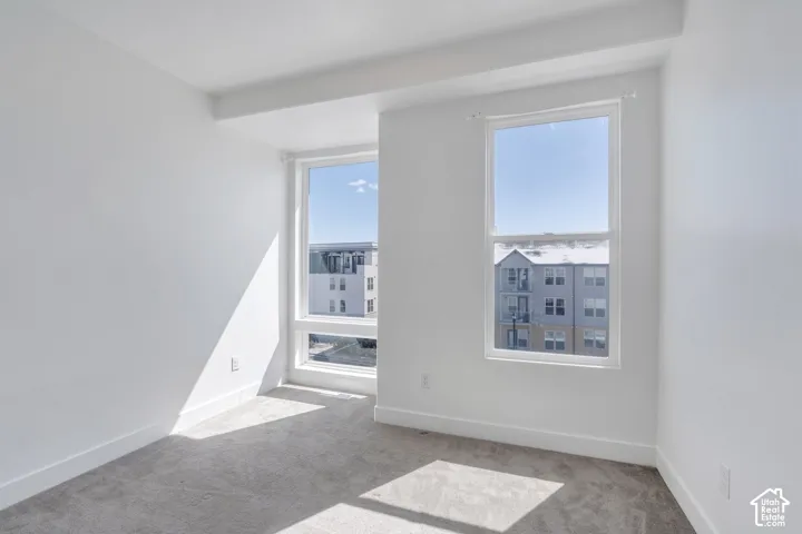 Two large windows providing abundant natural light, neutral wall colors, and gray carpet flooring