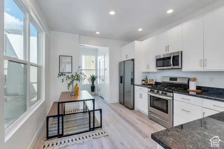 White shaker cabinetry, stainless steel appliances, dark stone countertops, wood-finish flooring, and recessed lighting