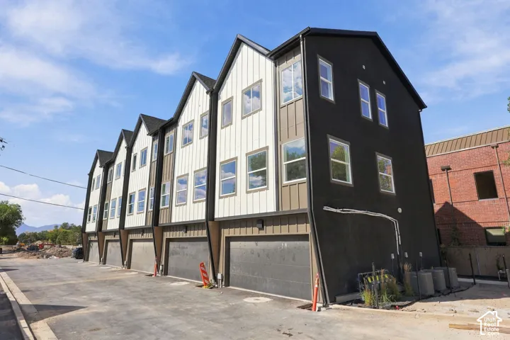 Modern multi-unit residential building featuring contemporary architectural design with steeply pitched gable rooflines, mixed exterior cladding in black and light-tone vertical siding, expansive multi-pane windows, and ground-level garage parking with co