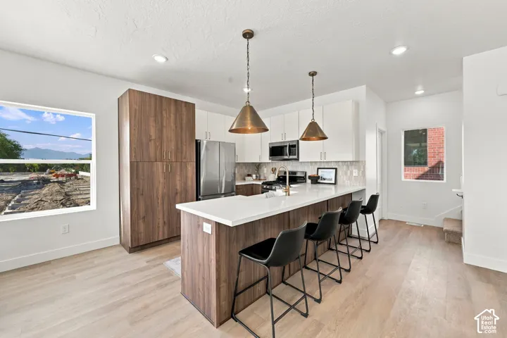 Open-concept kitchen featuring light wood-finish flooring, two-tone cabinetry with white upper and wood-finish lower cabinets, stainless steel appliances, and a central island with countertop seating