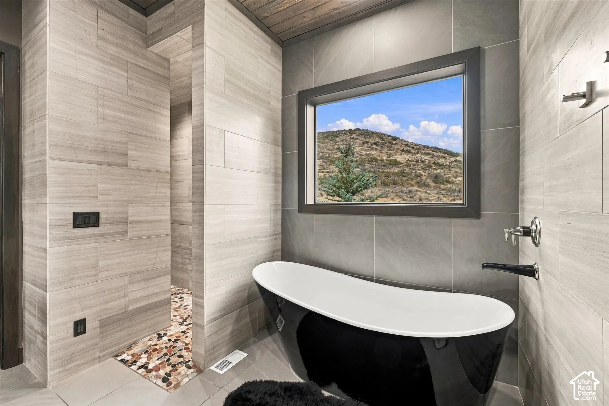 Freestanding black and white soaking tub, wall-mounted tub filler, and a large window with natural scenery