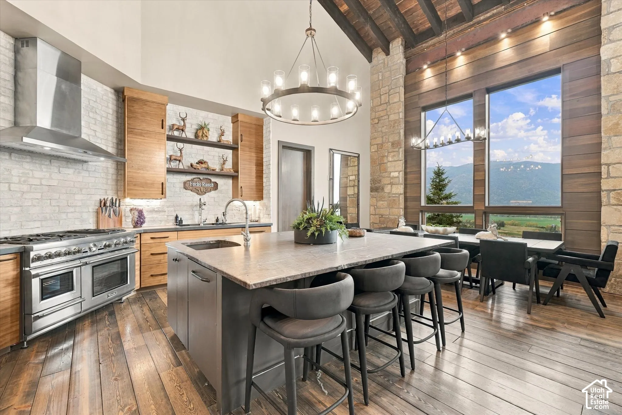 Gourmet kitchen featuring a large island with seating, stainless steel appliances, wood-finish cabinetry, and high ceilings with exposed wood beams