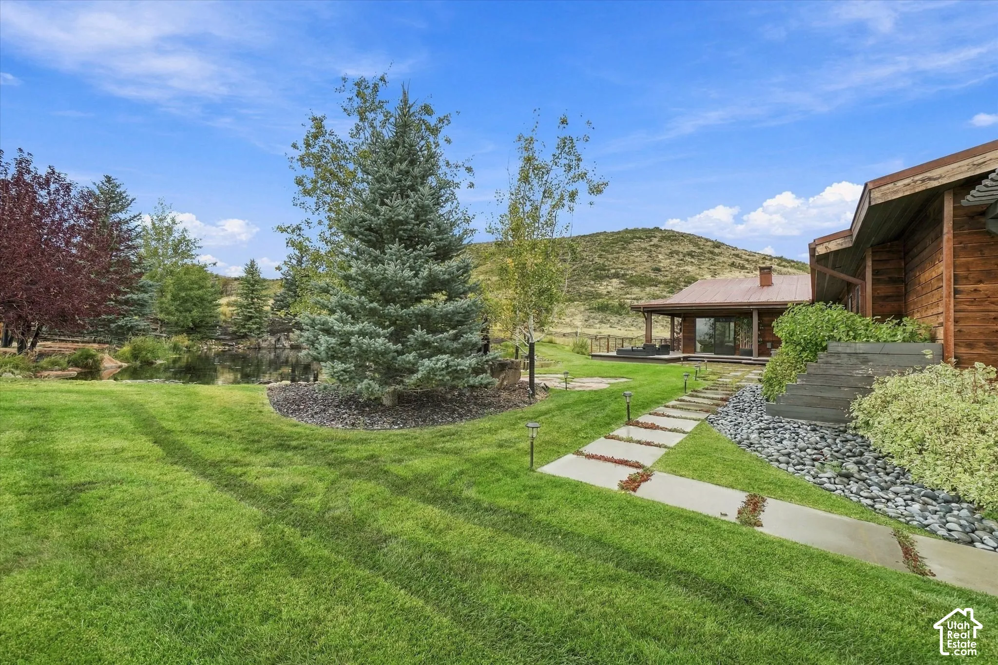 Expansive lawn, mature trees, decorative rock landscaping, stepping stone pathway, and a secluded patio with a covered porch