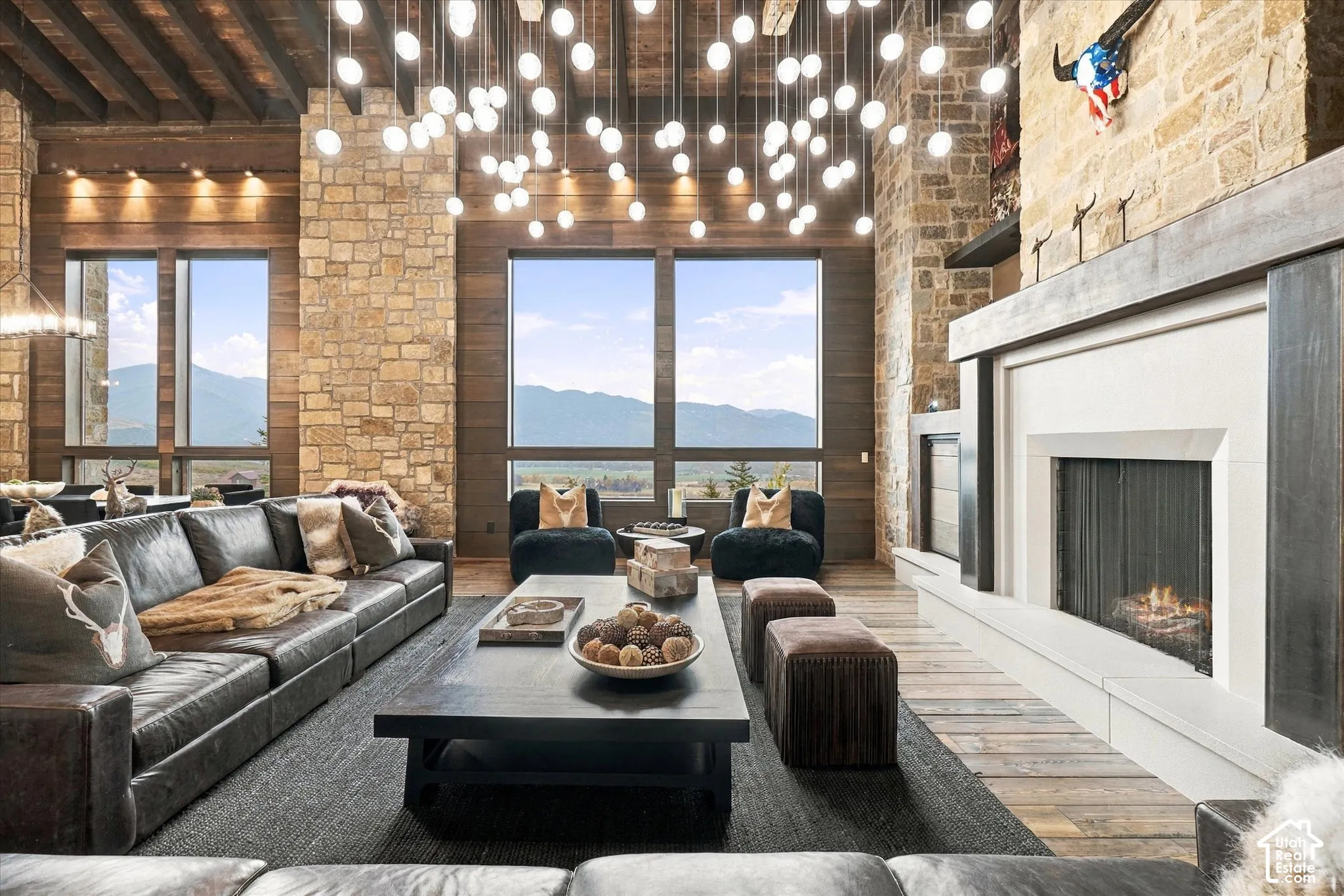 Expansive living space featuring a stone accent wall, large windows, wood-finish flooring, a contemporary fireplace, and a striking multi-light pendant fixture