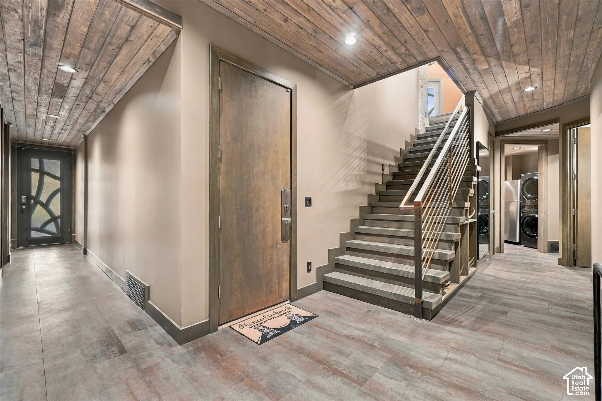 Wood-finish flooring throughout, featuring a staircase with metal railings and a built-in laundry area