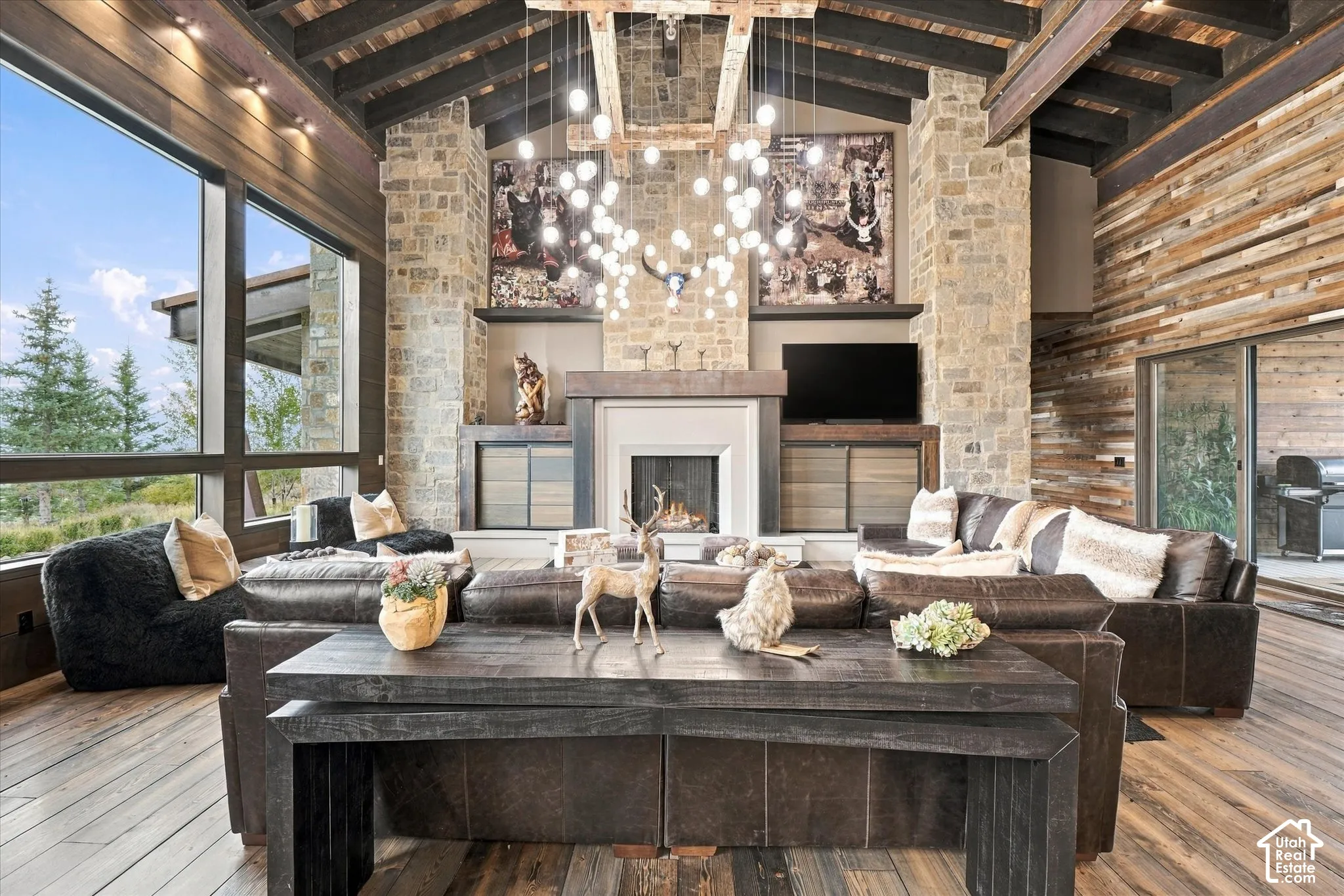 Stone fireplace with a mantel, exposed wood ceiling beams, wood-finish flooring, and expansive windows