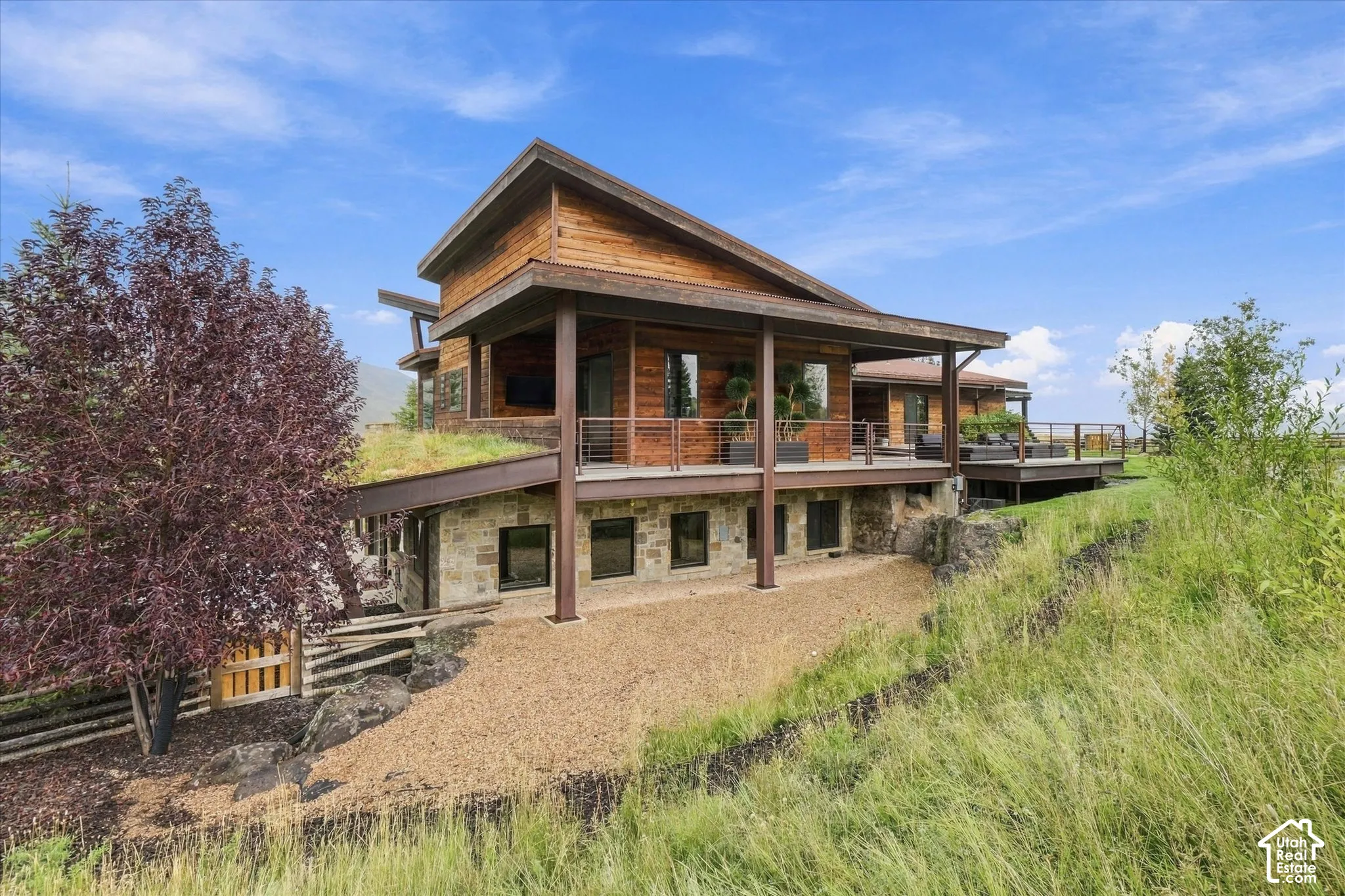 Multi-level exterior featuring wood siding, stone foundation, a green roof, and an expansive outdoor deck with metal railings