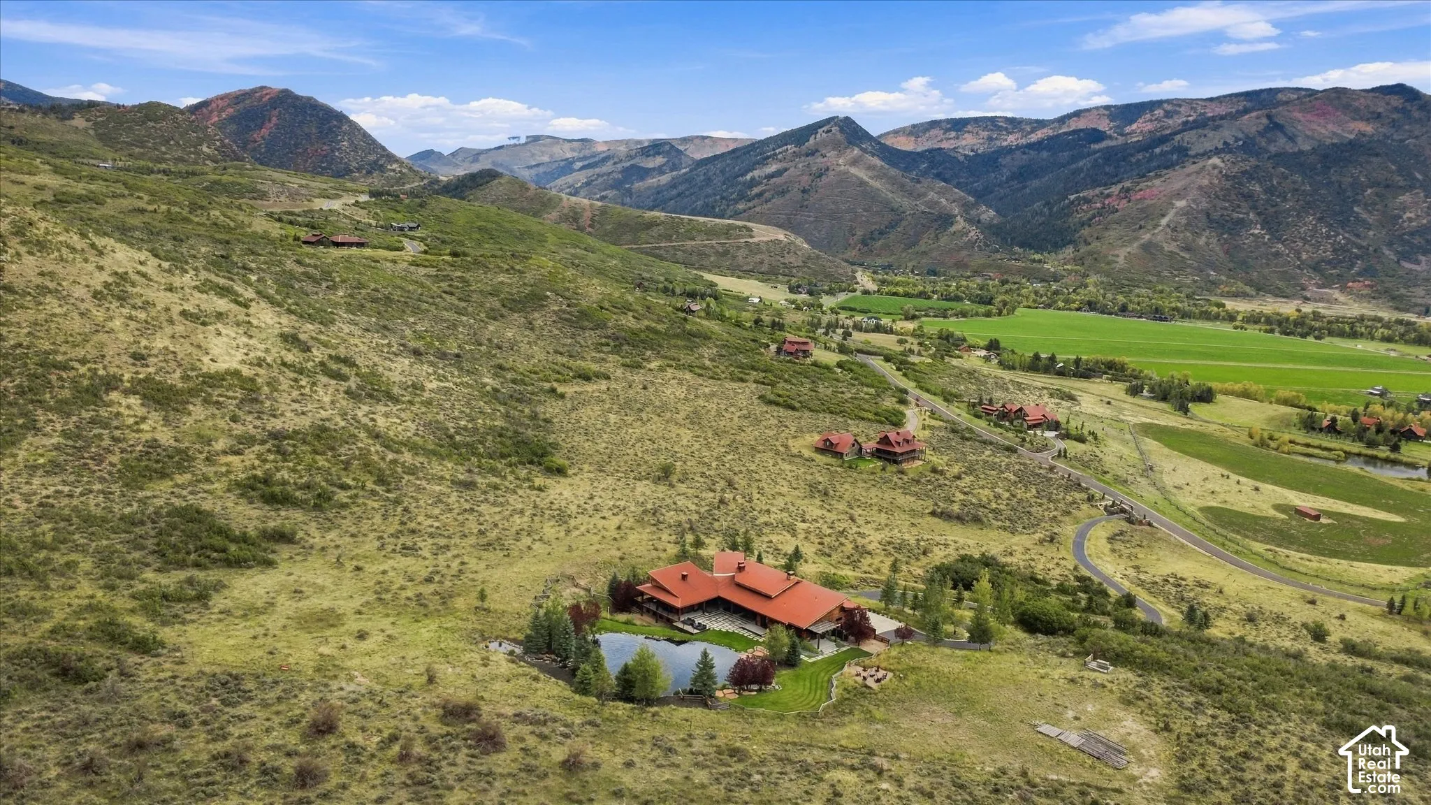 Expansive property featuring a red-roofed residence, a private pond, and surrounding hillsides