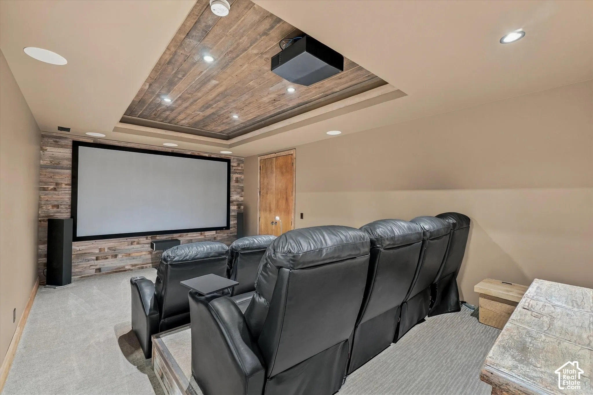 Dedicated media room featuring a large projection screen, wood-finish accent wall, wood-finish ceiling treatment, recessed lighting, and integrated ceiling speakers