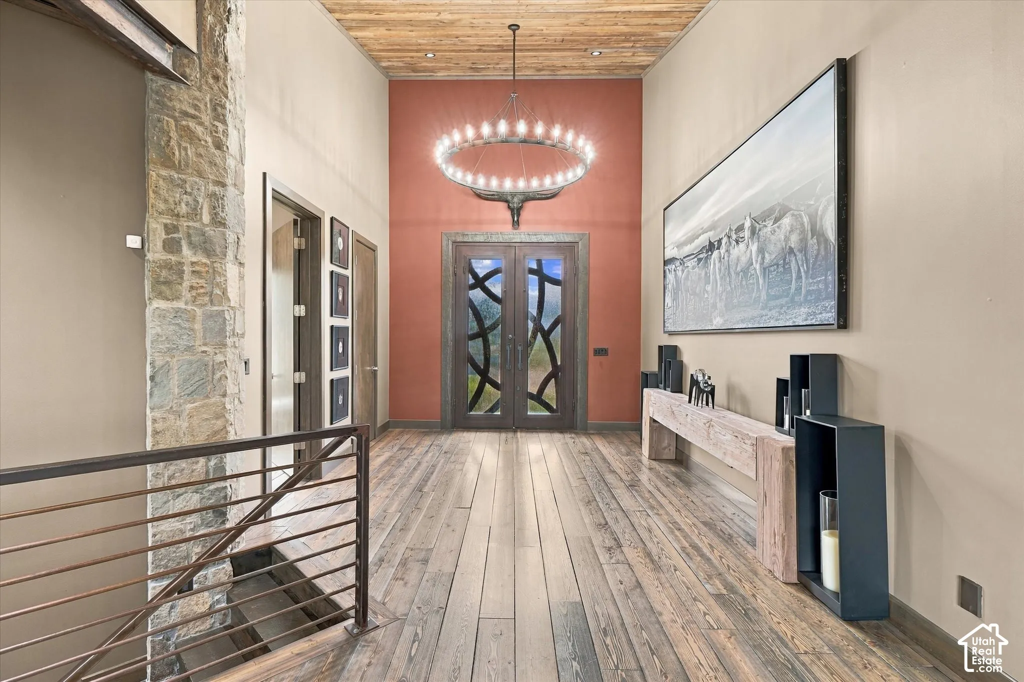 Vaulted ceiling with wood-finish planks, wood-finish flooring, stone accent wall, custom double entry doors with decorative glass, and a metal-railed staircase