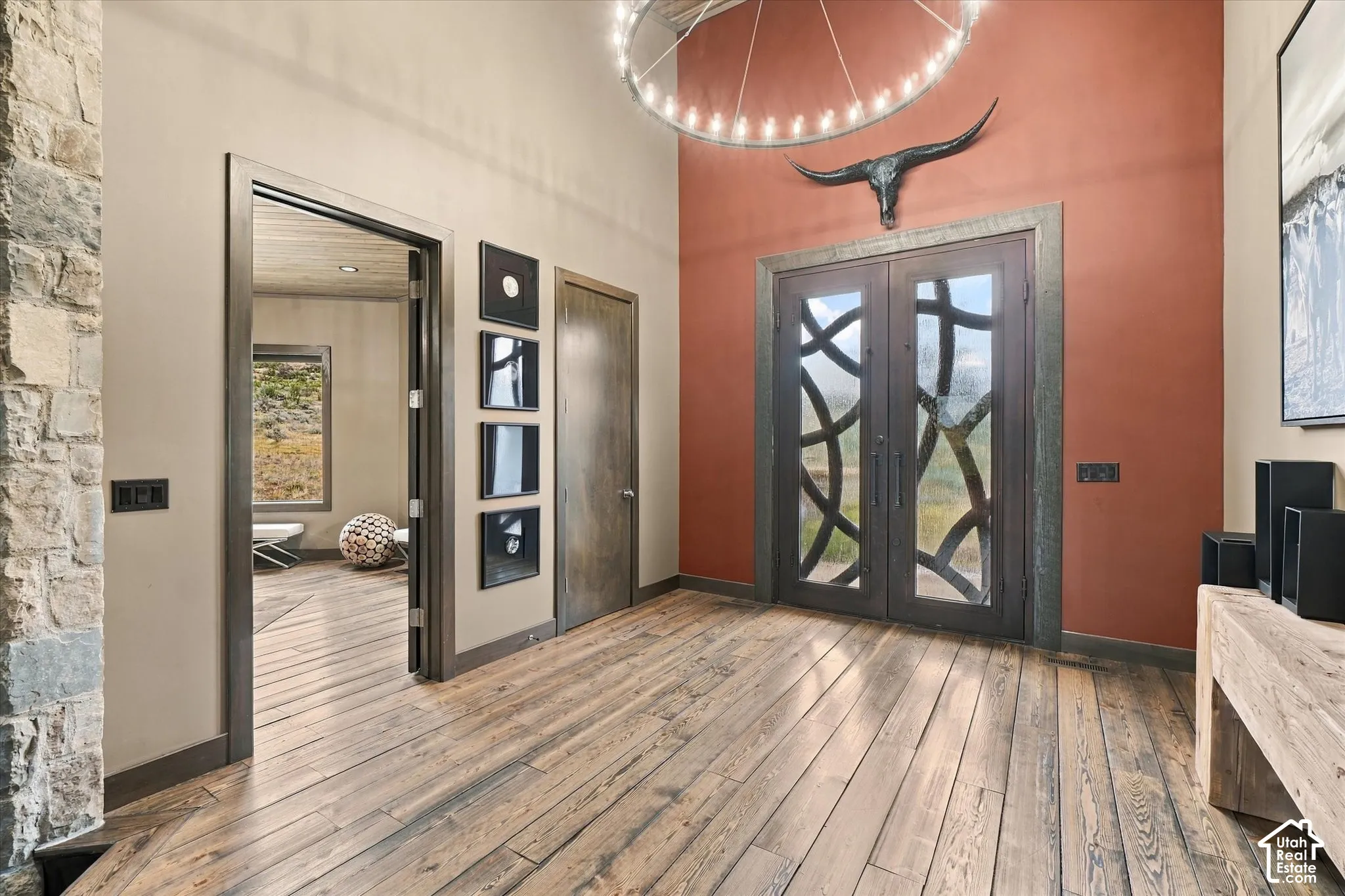 Wood-finish flooring throughout, double entry doors with decorative ironwork, stone accent wall, high ceilings, and a circular chandelier