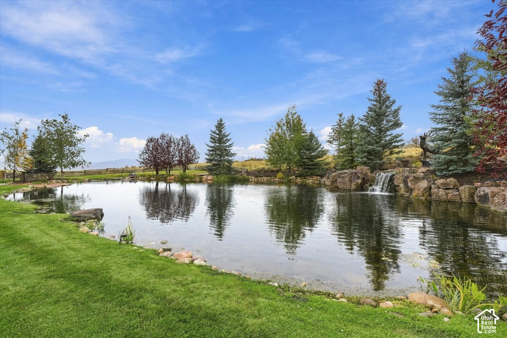 Expansive water feature with a rock waterfall, surrounded by mature trees and manicured lawn