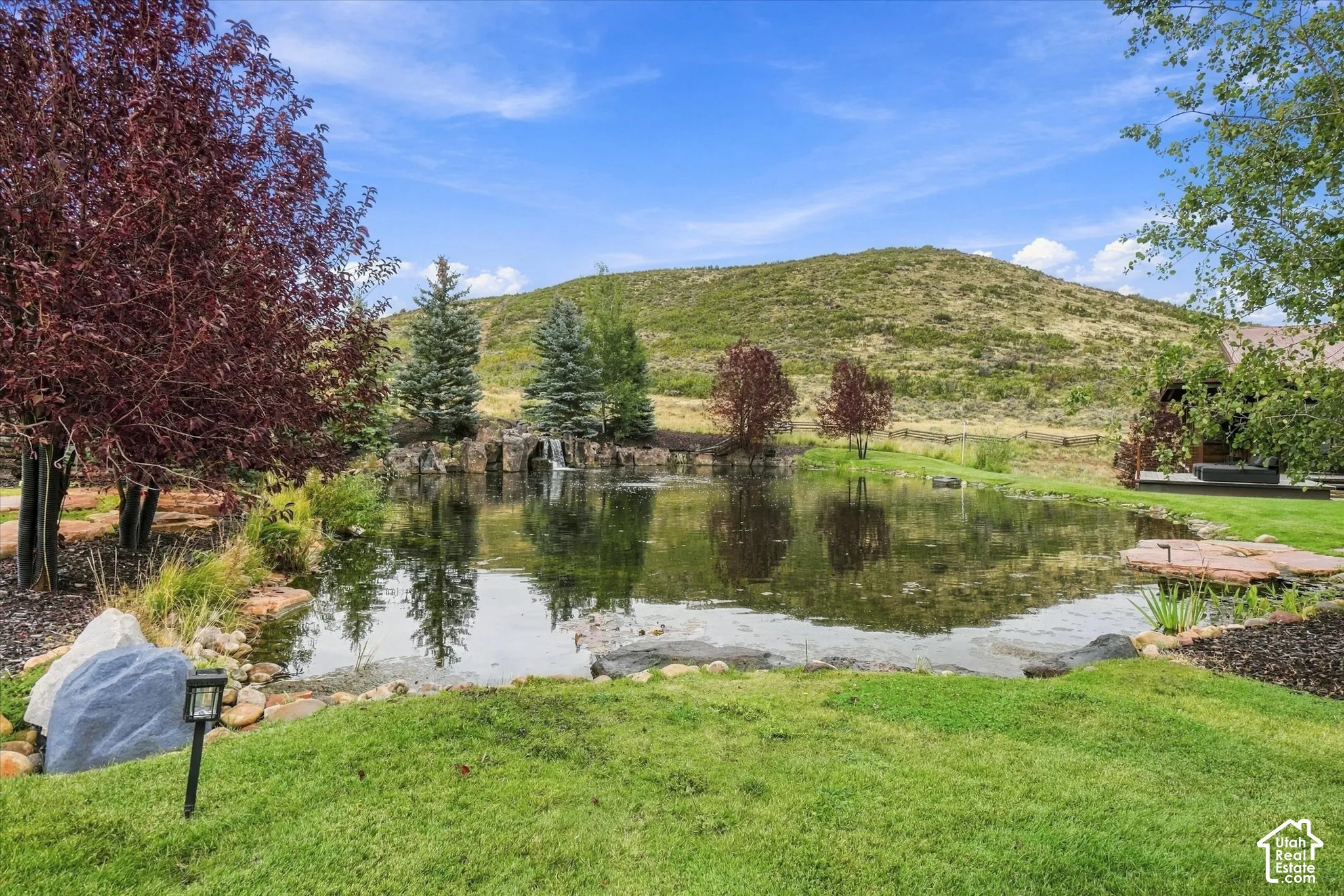 Expansive pond with a rock-lined edge, integrated waterfall feature, and surrounding mature trees