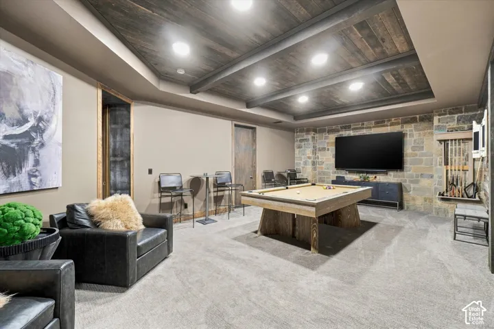 Stone accent wall with built-in media center, coffered wood-finish ceiling, recessed lighting, and carpeted flooring