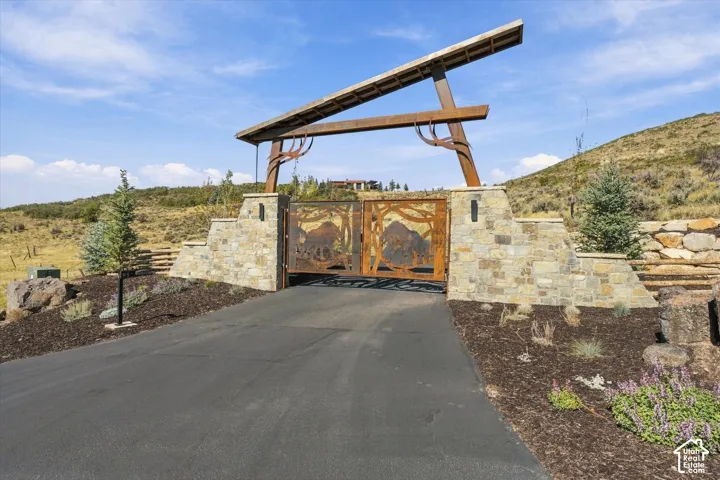 Asphalt driveway leading to a custom metal and wood-beam entry gate