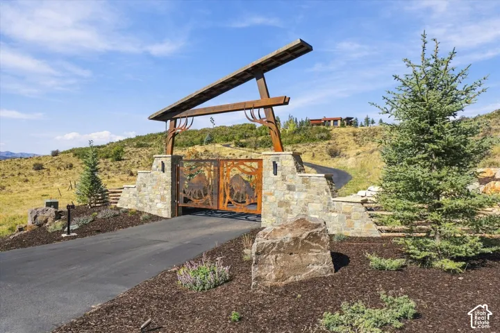 Stone pillar entry with custom metal gates, paved driveway, and natural landscaping
