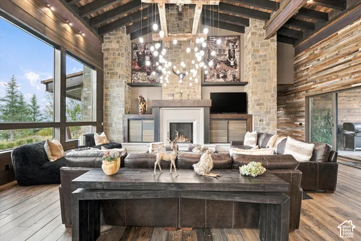 Stone fireplace with a mantel, exposed wood ceiling beams, wood-finish flooring, and expansive windows