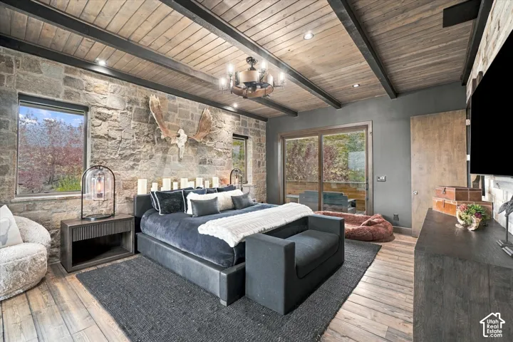 Wood-finish flooring, exposed wood beam ceiling, stone accent wall, sliding glass door to exterior, and wall-mounted light fixture