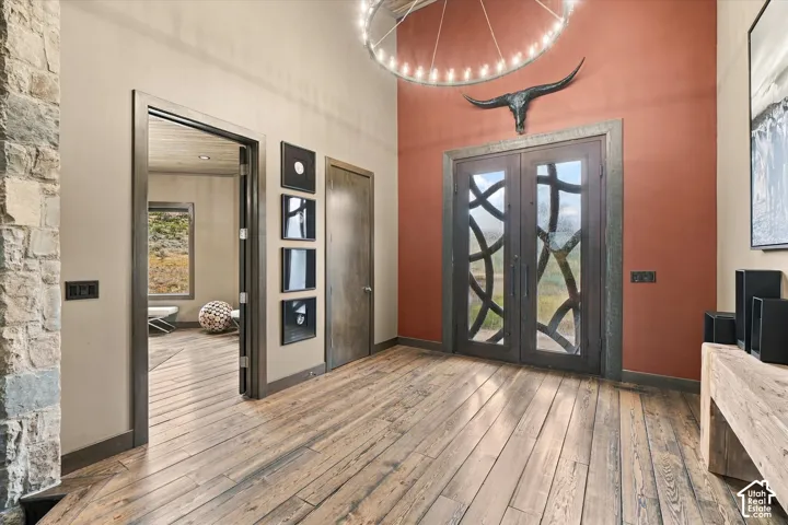 Wood-finish flooring throughout, double entry doors with decorative ironwork, stone accent wall, high ceilings, and a circular chandelier