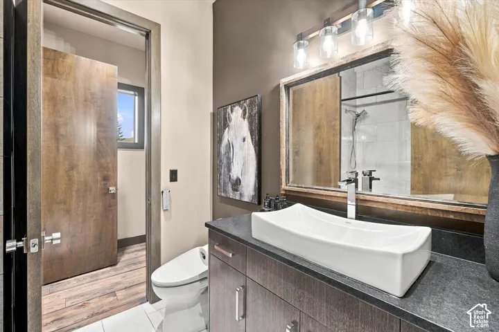Wood-finish bathroom door, white rectangular vessel sink, dark wood-finish vanity with drawer storage, sleek chrome faucet, and contemporary vanity lighting