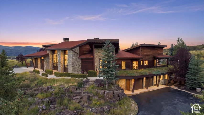 Stone and wood siding exterior with a red roof, multiple garages, and a green roof section